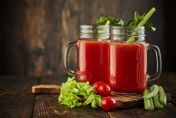 Two glasses with fresh tomato juice, celery, parsley and ripe tomatoes on dark brown wooden background with copy space. Healthy beverage, vegetable juice - Φωτογραφία, εικόνα