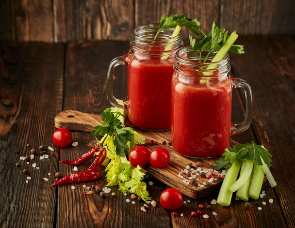 Two glasses with fresh tomato juice, celery, parsley, spices and ripe tomatoes on dark brown wooden background with copy space. Healthy beverage, vegetable juice - Fotó, kép