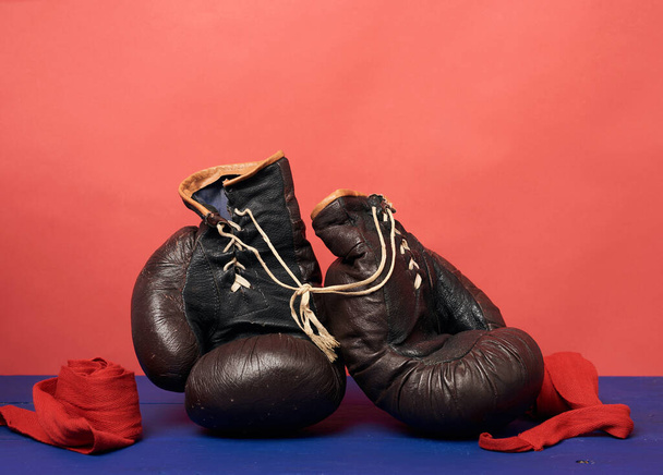 brązowe skórzane rękawice bokserskie vintage na czerwonym tle, sprzęt sportowy, przestrzeń do kopiowania - Zdjęcie, obraz