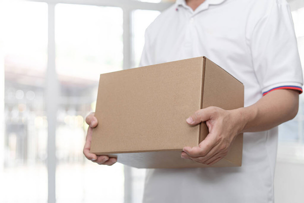 Чоловік-доставка в білій сорочці тримає картонну коробку на домашньому тлі: концепція сервісного карантину пандемії коронавірусу 2019-москва
 - Фото, зображення