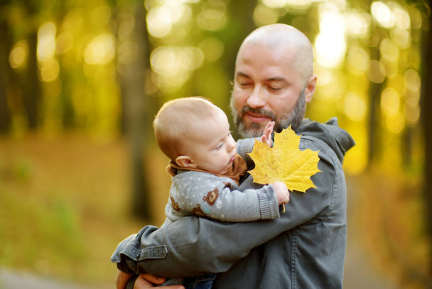 Cute little baby boy in his fathers arms. Dad and son having fun on sunny autumn day in city park. Adorable son being held by his daddy. - Фото, зображення
