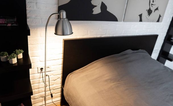 Steel downbridge floor lamp with a long arm and opaque shade near bed in black and white modern bedroom. Metal Task Lamp with an adjustable reading light. Stylish bedside lamp in scandinavian interior - 写真・画像