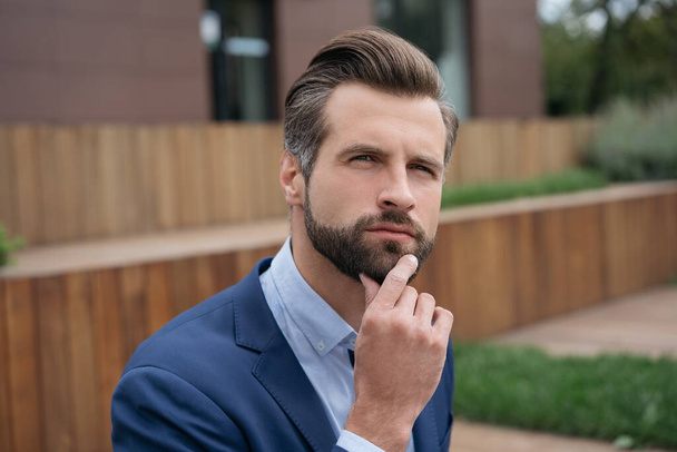 Primer plano retrato de hombre de negocios guapo pensativo planificación de la puesta en marcha de negocios. Joven gerente barbudo buscando una solución creativa al aire libre  - Foto, imagen