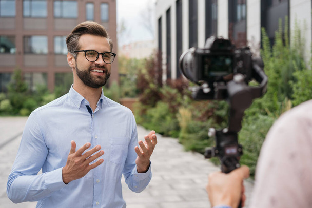 Handsome journalist or news reporter broadcasting on the street. Tv news, reportage concept. Portrait of confident smiling influencer live streaming outdoors  - Photo, Image