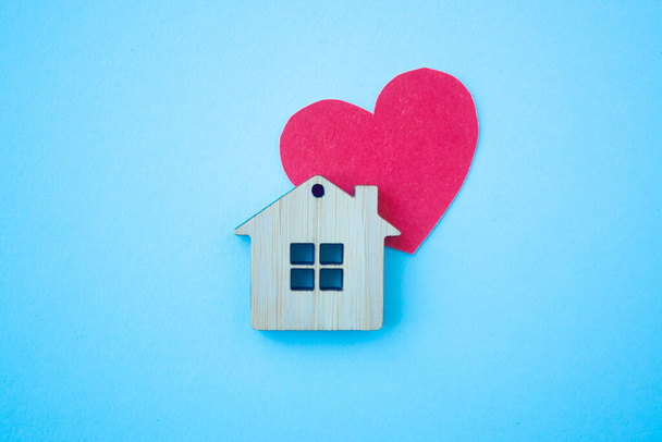 Dům lásky, pojištění a hypotéka, manželství a valentýnský koncept. Malý dřevěný dům hračka a papír srdce tvar na modrém pozadí horní pohled - Fotografie, Obrázek