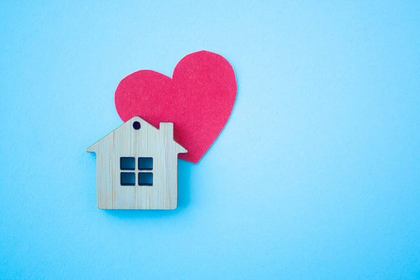 Love home, insurance and mortgage, marriage and valentine concept. Small wooden house toy and paper heart shape on blue background top view copyspace - Zdjęcie, obraz