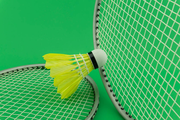 Badminton rackets and yellow feathered shuttlecocks on green background in a close up view - Fotografie, Obrázek