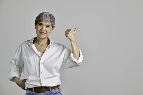 Mulher asiática de meia idade apontando os dedos para cima no espaço vazio cópia para o texto isolado no fundo branco - Foto, Imagem