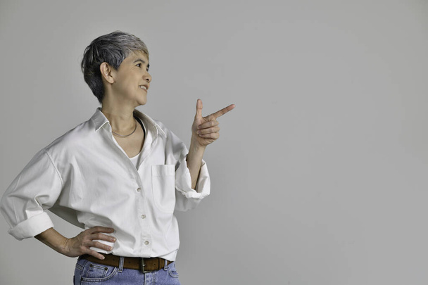 Asiatin mittleren Alters zeigt mit dem Finger auf leeren Kopierraum für Text auf weißem Hintergrund - Foto, Bild