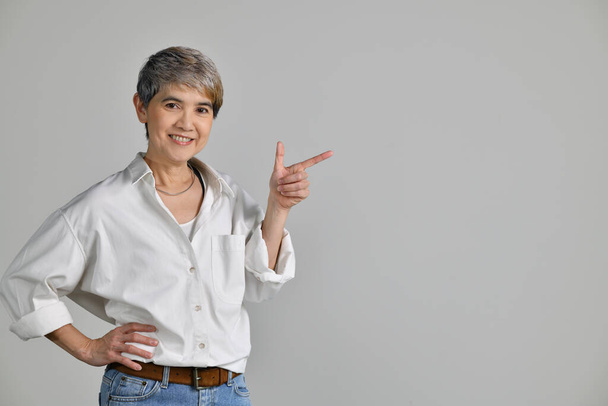 Mujer asiática de mediana edad señalando con los dedos hacia arriba en el espacio de copia vacío para el texto aislado sobre fondo blanco - Foto, imagen