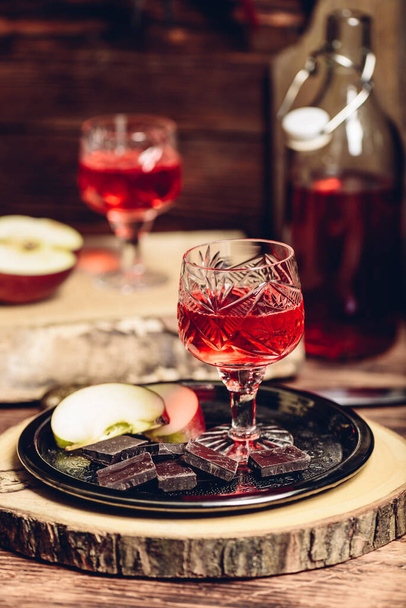 Glass of homemade redcurrant nalivka with apple slices and chocolate on metal plate - Fotó, kép
