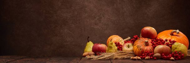 Festive autumn still life with pumpkins, apples, red berries, nuts, rye ears on dark wooden surface on brown background with copy space. Concept of autumn harvest, happy Thanksgiving  day or Halloween - Foto, Bild