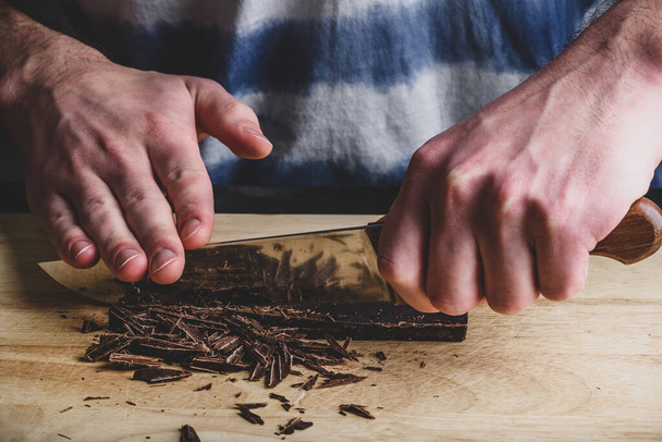 Roughly chopping dark chocolate bar with knife - Fotó, kép