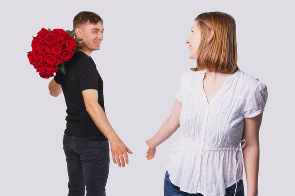 Jeune couple debout au loin l'un de l'autre, petit ami tenant un gros bouquet de roses rouges sur son épaule pour donner à sa petite amie blonde. - Photo, image