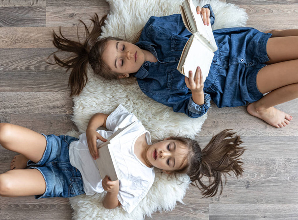 Two cute children reading books lying on the floor at home. - Foto, imagen