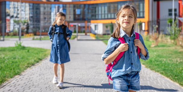 Ученики начальной школы. Девушки с рюкзаками возле здания на открытом воздухе. Начало уроков. Первый день осени
. - Фото, изображение