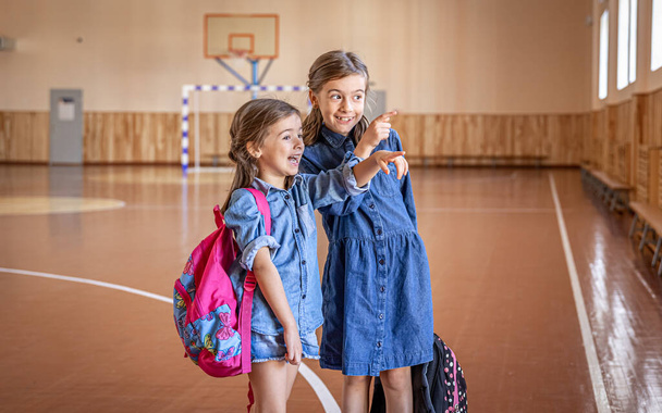 Маленькі дівчата, початкові школярки, з рюкзаками після школи в шкільному тренажерному залі
. - Фото, зображення