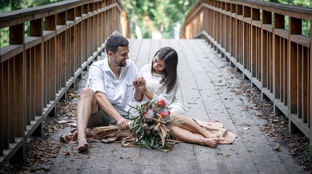 Девушка и молодой человек сидят на мосту и наслаждаются общением, свиданием на природе, историей любви. - Фото, изображение