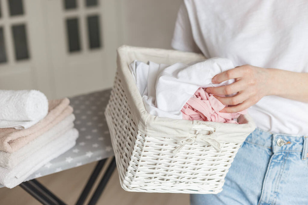 Wicker rustic basket with washed clothes in woman's hand ready to ironing. Close up view on basket in hands. Woman in living room - Photo, Image