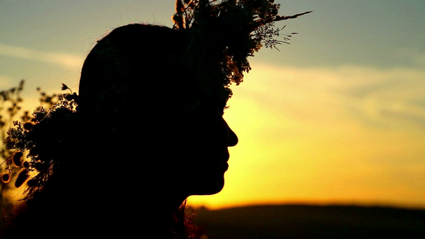 Portret van een meisje bij zonsondergang met een krans van wilde bloemen. - Video