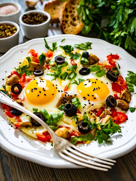 Sunny side up eggs with red bell pepper, tomatoes, chive and black olives on wooden table - Photo, image