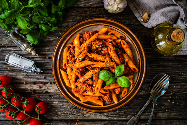 Penne with minced meat, tomato sauce, parmesan cheese, basil and vegetables served on wooden table  - Fotoğraf, Görsel