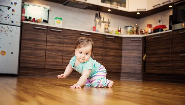 Cute smiling little baby girl crawling on the floor at kitchen. Seven month old infant child at home - Foto, Imagem