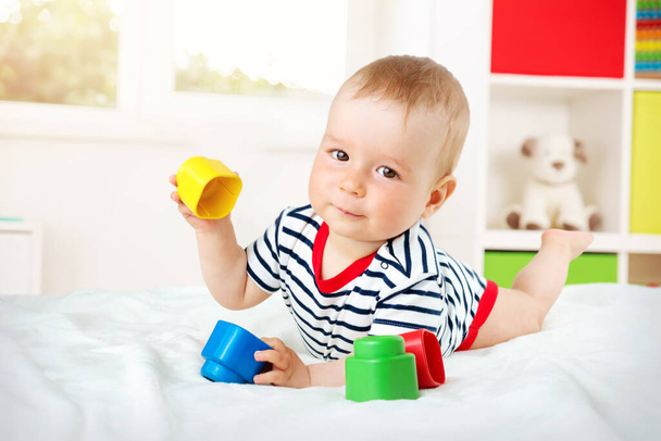 Nine month old baby lying in the bed on white blanket. Cute boy playing with cubes - Foto, imagen