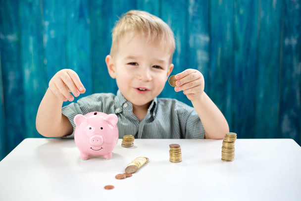 three years old child sitting st the table with money and a piggybank. Happy boy with euro coins - Foto, Imagen