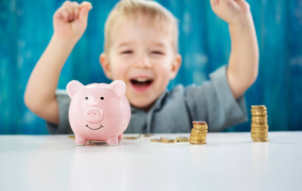 drie jaar oud kind zittend in de tafel met geld en een spaarvarken. Gelukkige jongen met euromunten - Foto, afbeelding