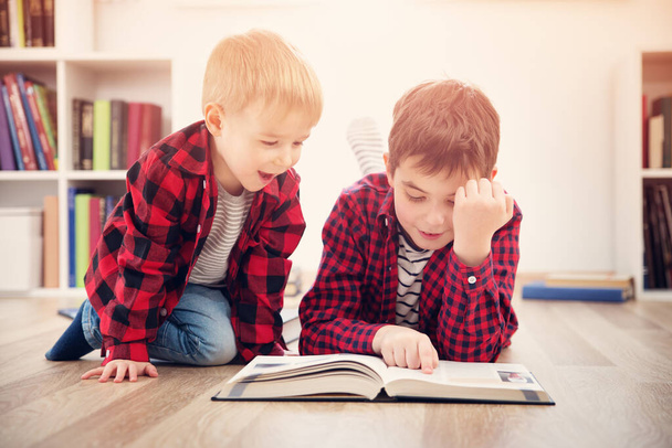 Three years old child and his older brother sitting among books at home. Curious boys reading in white room - Foto, Bild