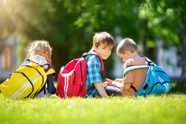 Children with rucksacks standing in the park near school. Pupils with books and backpacks outdoors - Fotografie, Obrázek