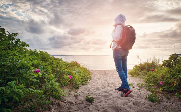 sea in sunset light. Woman in Lahemaa natural park coastal landscape with beautiful sky. Person with rucksack - 写真・画像
