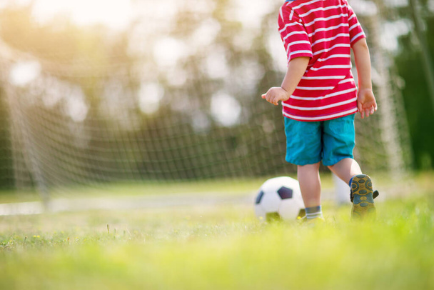 Little boy playting football on the field with gates. Active child in summer with ball - Photo, Image