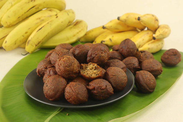 Reiskrapfen mit einem Teig aus Reismehl, Banane, Jaggery und gerösteten Kokosnussstücken. Traditioneller Snack aus Kerala, bekannt als Unni appam. Schuss auf Bananenblatt mit Banane im Hintergrund - Foto, Bild