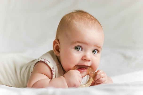Baby girl on her stomach with teether in the mouth - Fotoğraf, Görsel