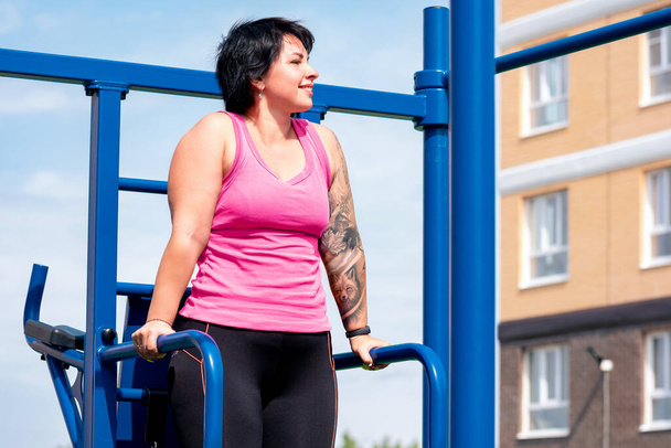 mujer joven realiza ejercicios al aire libre usando la máquina combinada de fitness de la calle - Foto, imagen