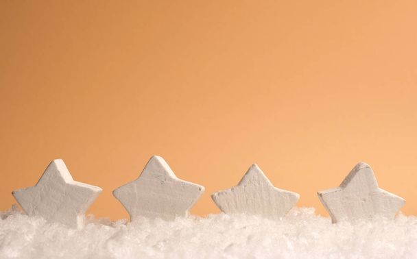 Four white wooden star shapes with snow on an orange paper background, space for text on top, seasonal or holiday background - Fotografie, Obrázek