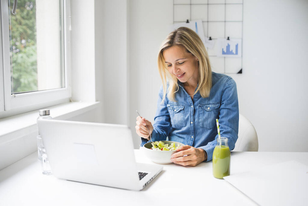 Pretty young business woman eating healthy salad in office - Zdjęcie, obraz