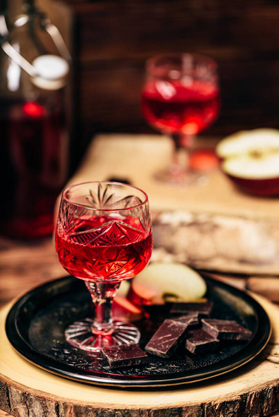 Glass of homemade redcurrant nalivka with apple slices and chocolate on metal plate - Foto, immagini