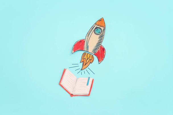 Painted rocket and open notebook over pastel blue background - Фото, изображение