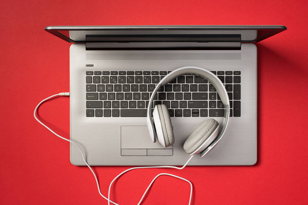 Photo aérienne d'un ordinateur portable gris et d'écouteurs isolés sur fond rouge - Photo, image