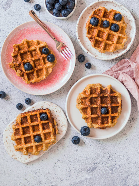 Easy healthy gluten free oat waffles with copy space. Plates with appetizing homemade waffles with oat flour decorated blueberries, on light gray cement background. Vertical. Top down view or flat lay - Foto, Imagen