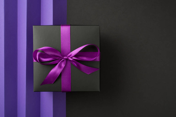 Top view photo of black giftbox with purple ribbon bow on isolated bicolor violet and black background with copyspace - Foto, imagen