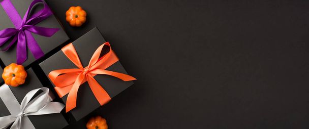 Top view photo of three black gift boxes with violet orange and white ribbon bows and small pumpkins on isolated black background with copyspace - Photo, Image