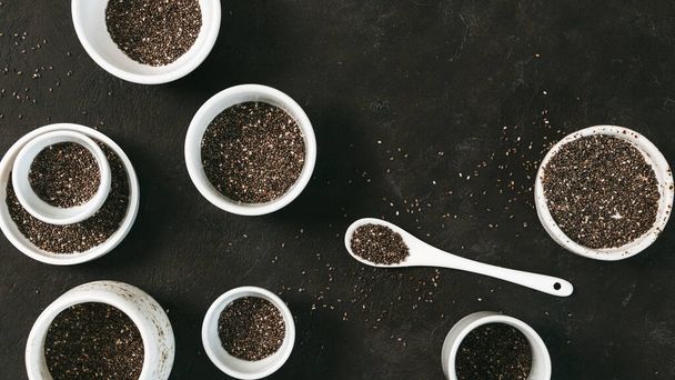 Organic chia seeds on black tabletop. Set of small bowls with organic chia seed. Superfood concept. Copy space. Top view or flat-lay. - Photo, Image