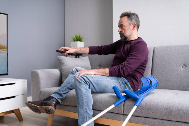 Injured Man With Broken Leg And Crutches Watching TV - Fotó, kép