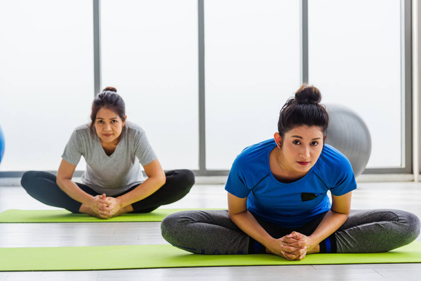Two Asian women sporty attractive people practicing yoga lesson together, working out at the fitness GYM, Young and senior female exercising do yoga in yoga classes, sport healthy lifestyle - Foto, Imagem