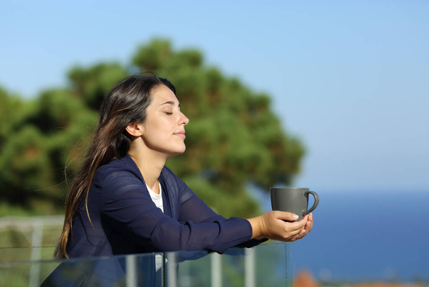Relaxed woman with closed eyes holding coffee mug in a hotel balcony on the beach - Foto, Imagen