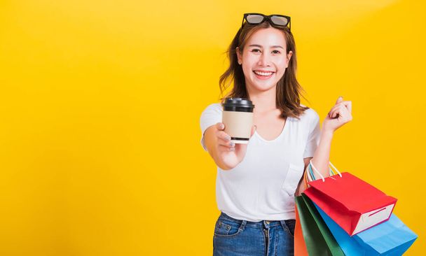 Portrait Asian Thai beautiful happy young woman smiling hold shopping bags multi-color and take away coffee cup her looking to camera, studio shot isolated on yellow background, with copy space - Fotografie, Obrázek